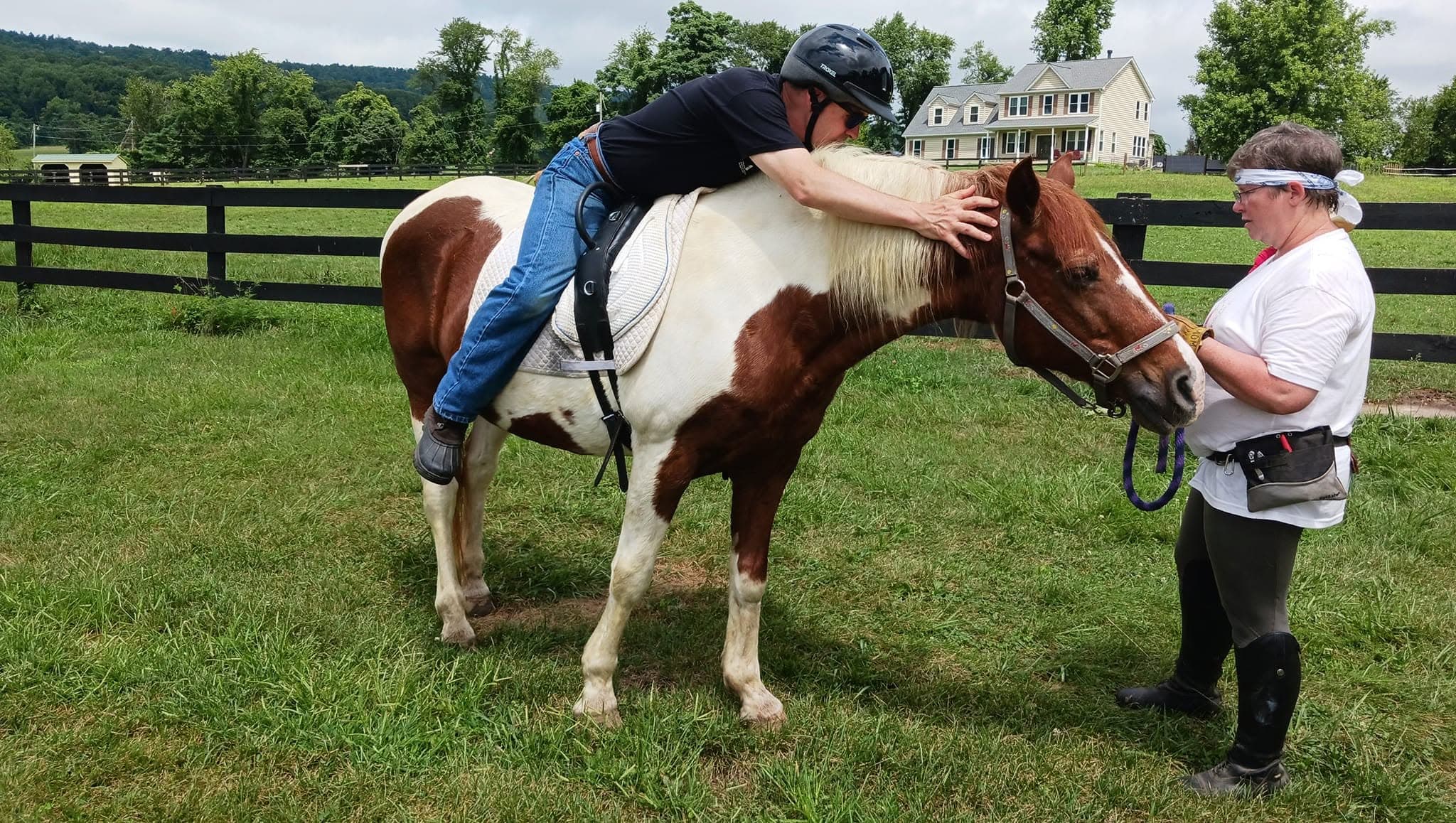 A helmeted rider leans toward a paint horse, with a handler beside them at Eagle’s Nest